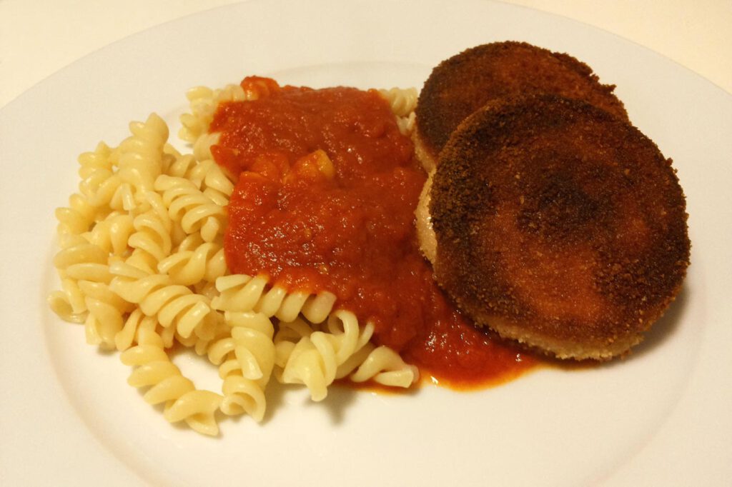 DDR-Jägerschnitzel aus panierter Jagdwurst mit Spirelli und Tomatensoße auf dem Teller