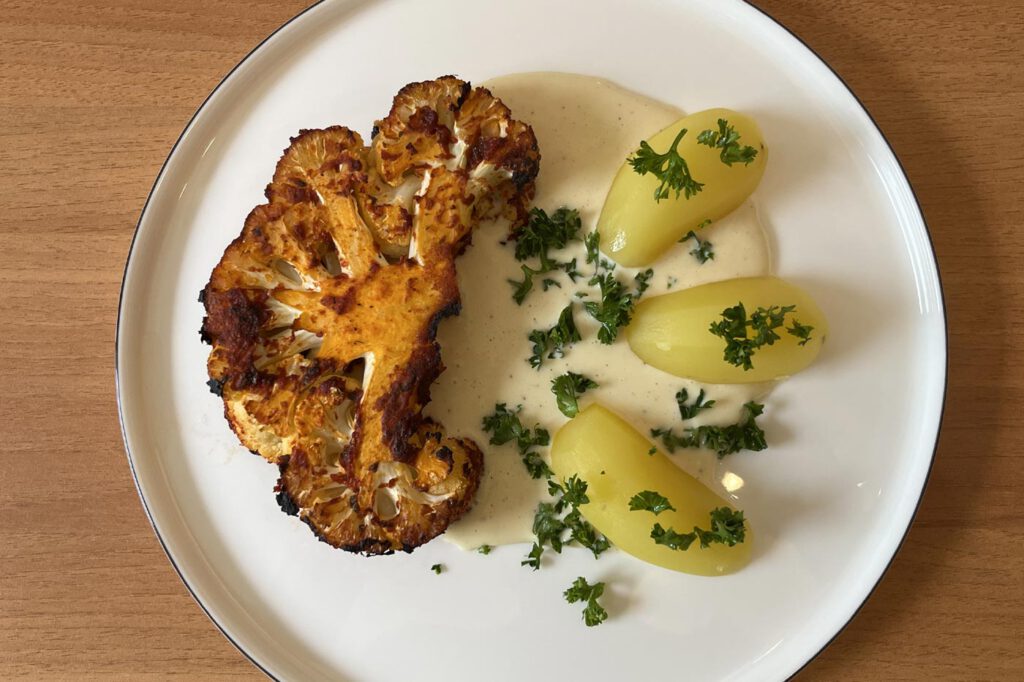 Mariniertes Blumenkohlsteak mit heller Soße und Petersilienkartoffeln auf einem weißen Teller